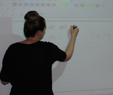 While reviewing the homework, Ms. Corrigan instructs her students on how to complete the problem.