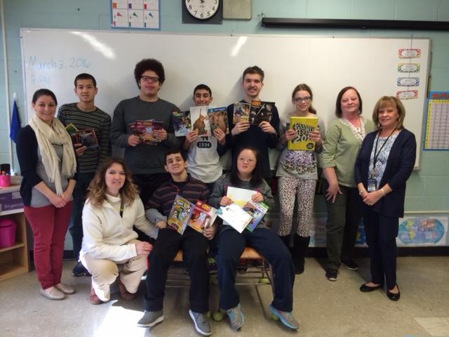 Ms. Motola and her special education class pose with their newly attained books from Ms. Newman, the president of the reading club and E. Commerce Scholastic, Inc.