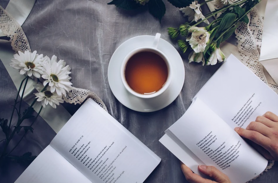 An image of a person with a poetry book and a cup of tea in front of them