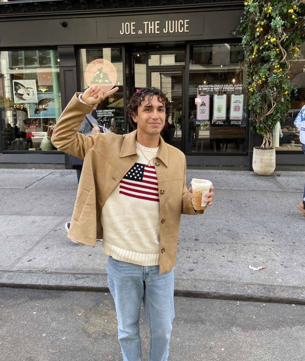 Journalist Joseph Torres dressed in a Fall outfit poses in front of a shop