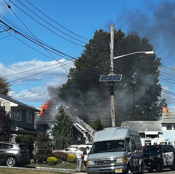 There is a huge fire that is taking place inside of a house. It is located near trees and produced a lot of smoke.