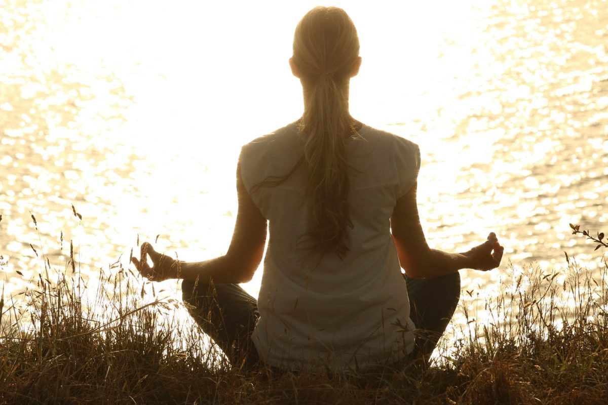 A girl is meditating alone while she is sitting on grass. This is an example of quality time. 