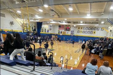 In Colonia High Gym, the Patriots warm up for the basketball game. Students fill the student section behind the backboard.