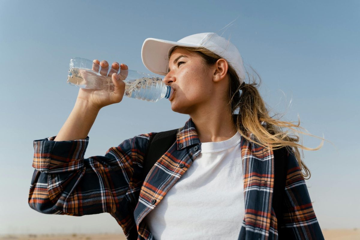 This is a picture of a female standing outside sweating. She is drinking water out of clear water bottle to hydrate herself.